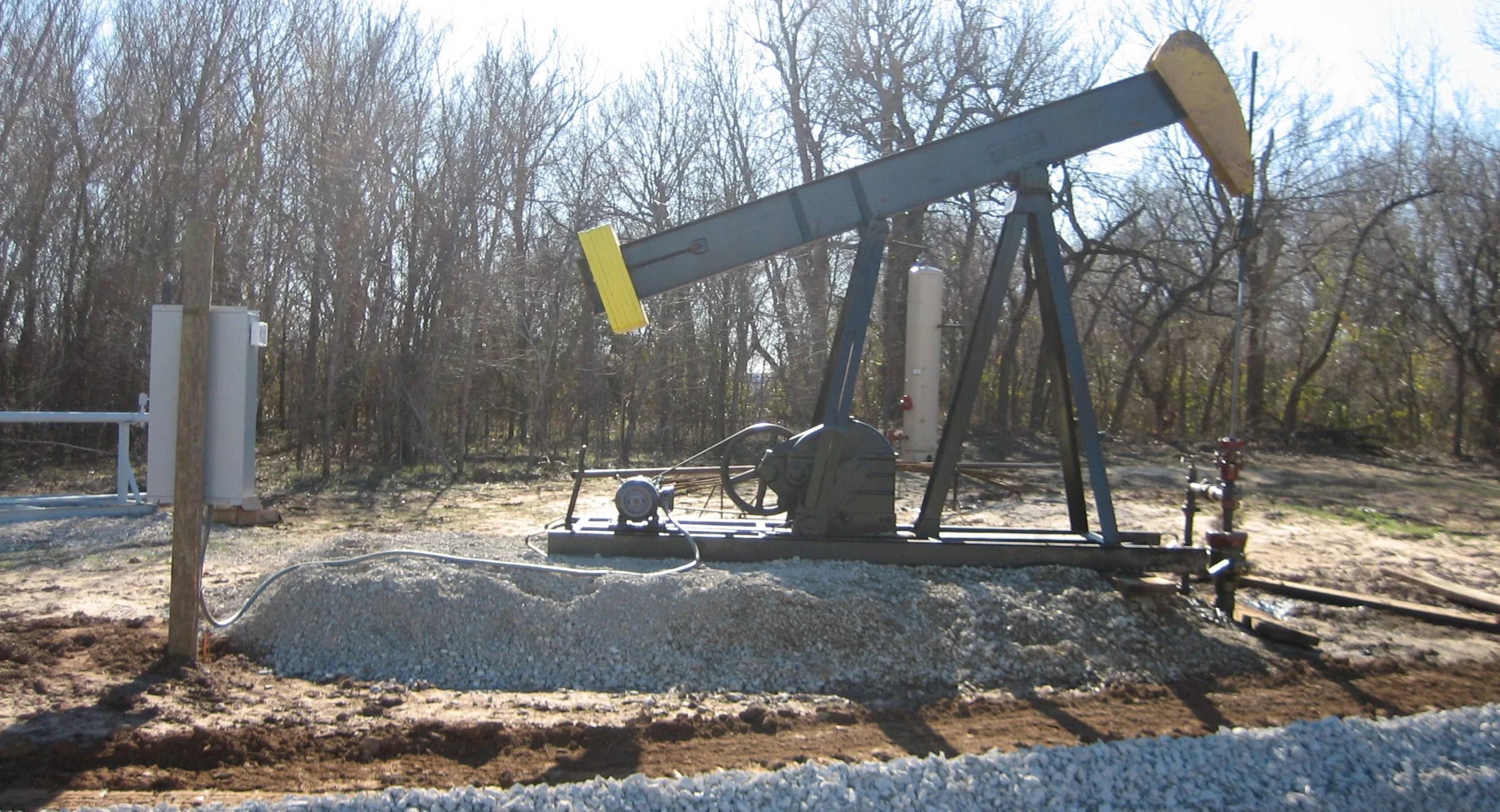 Pumpjack operating on a cleared lease location near wooded acreage
