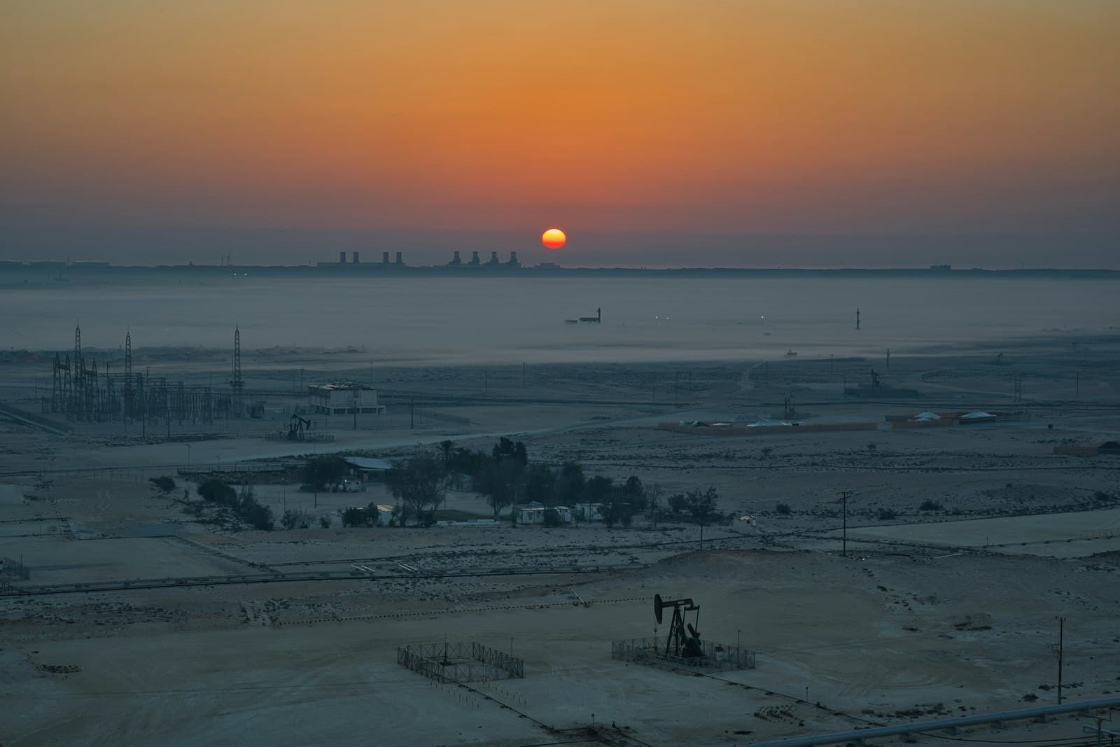 Pumpjacks at sunrise over an industrial oilfield landscape